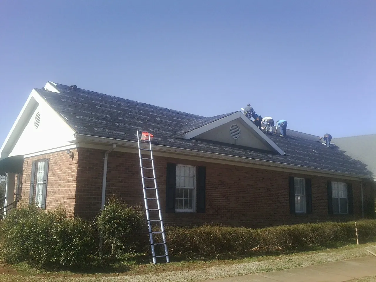 Crew tearing shingles off a brick ranch roof with a ladder set — Emergency Roof Repair work by our crew in Pollocksville