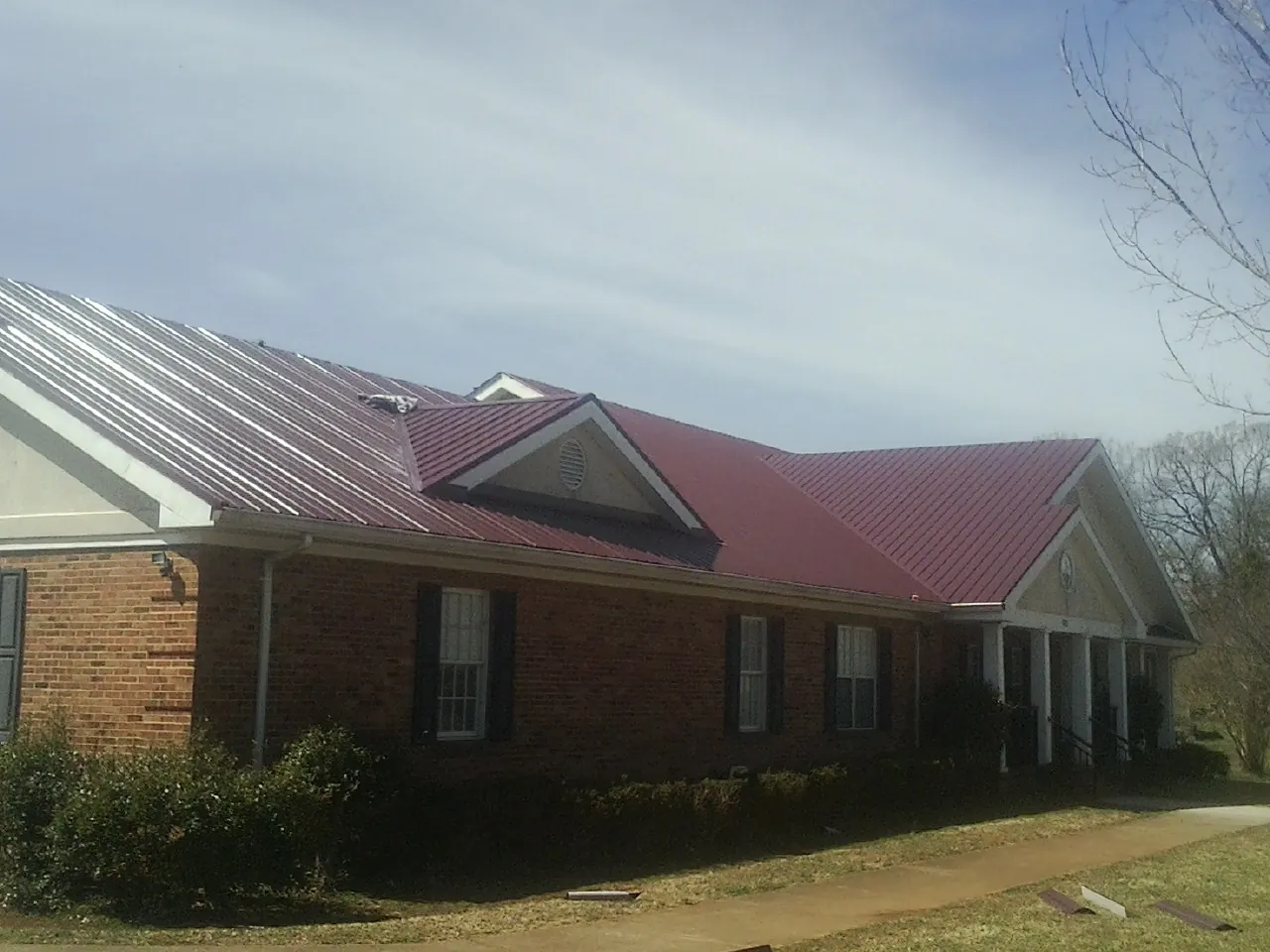 Red metal roof with gabled entries on a long brick building, from a Hail Damage Roof Repair job in Pollocksville