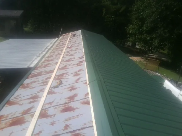 Old rusted panels beside newly installed green metal roofing — Wind Damage Roof Repair by Roofing Brothers in Pollocksville