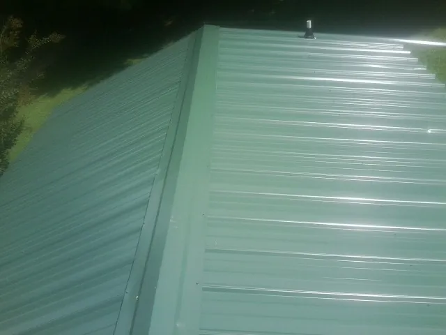 New green metal panels meeting at the ridge of a roof — Flat Roof Repair work by our crew in Pollocksville