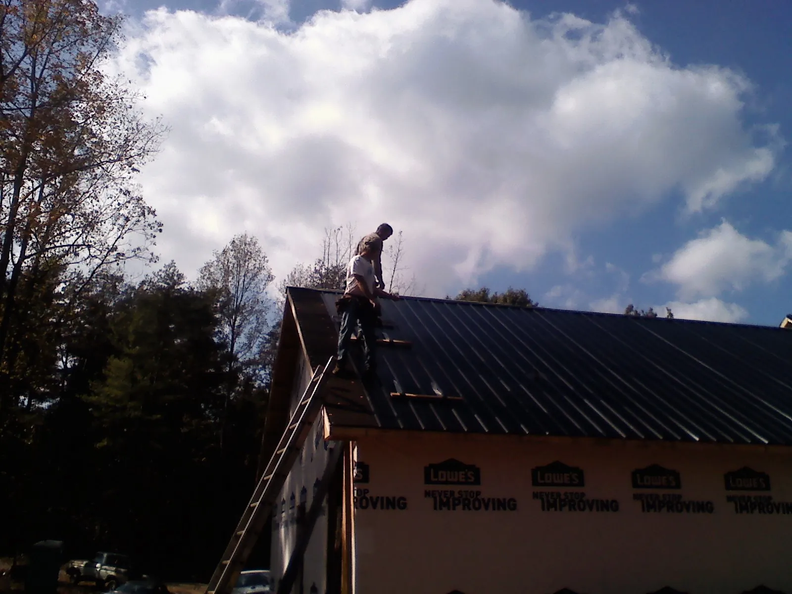 Roofer fastening dark metal panels high against a cloudy sky, from a Roof Inspection job in Pollocksville